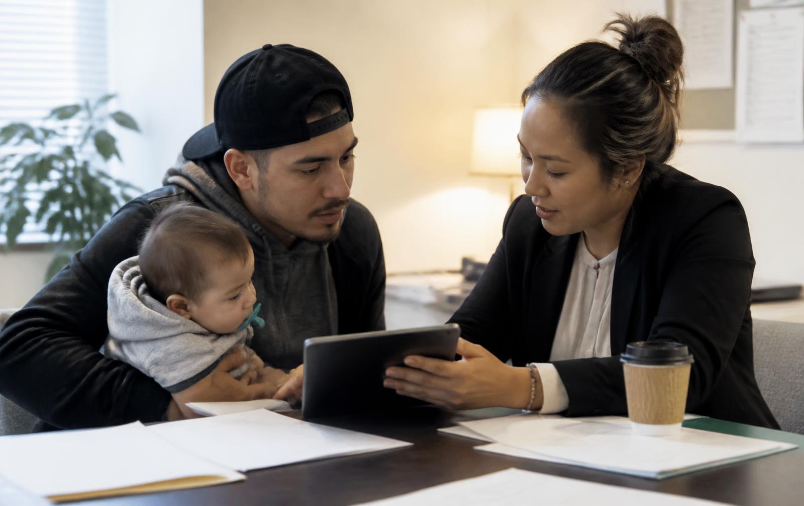 A THA caseworker helping a father holding his baby fill out a housing application